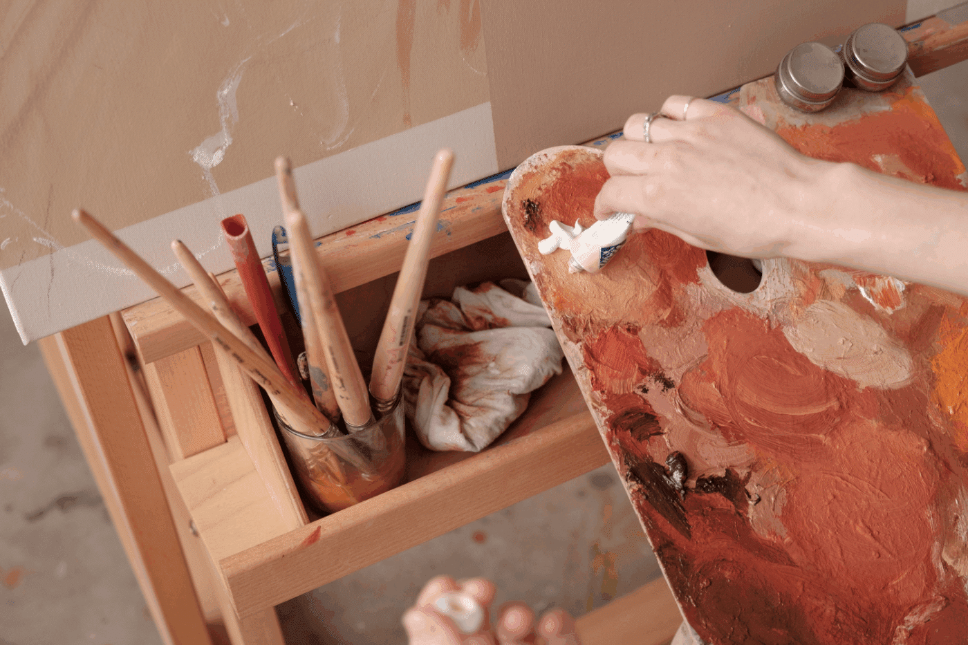 photo of an artist placing paint on a pink board in front of a an art stand.