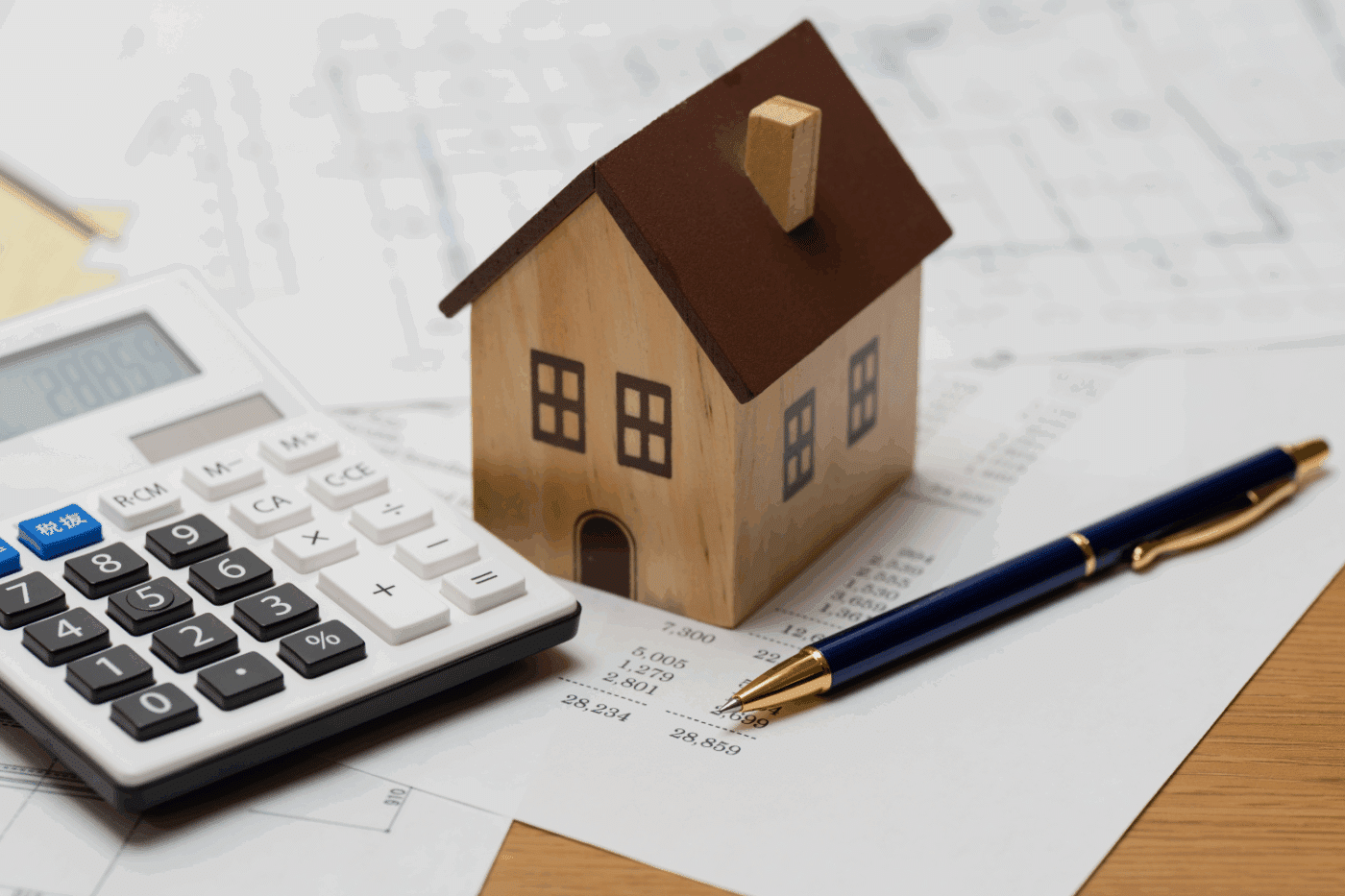 photo of a model house, featuring a pen and calculator on a balance sheet