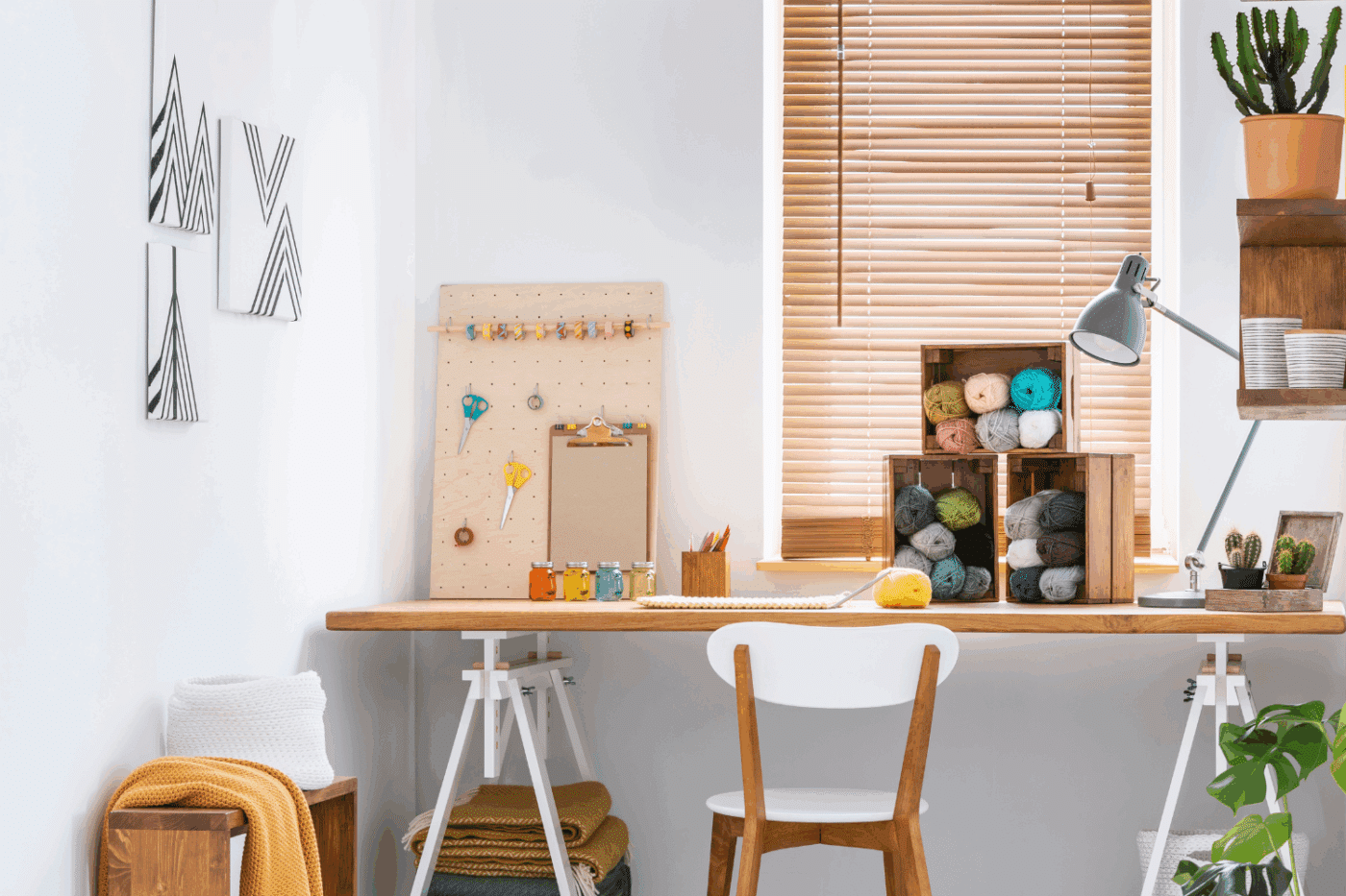 photo of a desk in front of a window with yarn and other craft supplies on the walls and desk