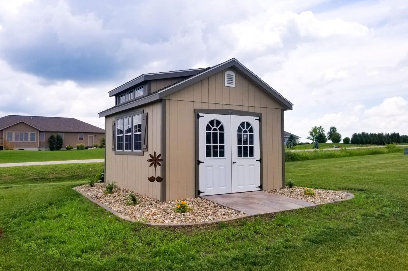 photo of a southern classic style dark tan with grey trimmed shed landscaped with gravel stones and a paver walkway to two white door entry way.